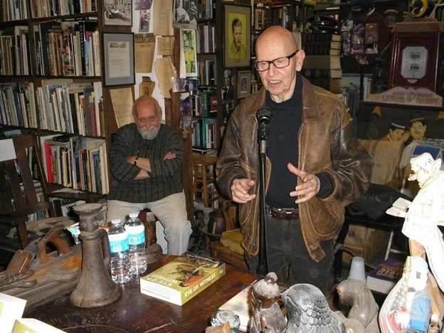 David Antin talking while Jerome Rothenberg listens in the background (photo by 
